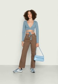 Top cropped de mangas longas azul claro, calças largas castanhas, bolsa azul e ténis cinzentos com detalhes brancos. Texturas suaves e design ajustado.