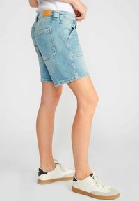Shorts en denim bleu clair avec une coupe droite, des poches avant et deux poches arrière. Assortis à des baskets blanches et noires.