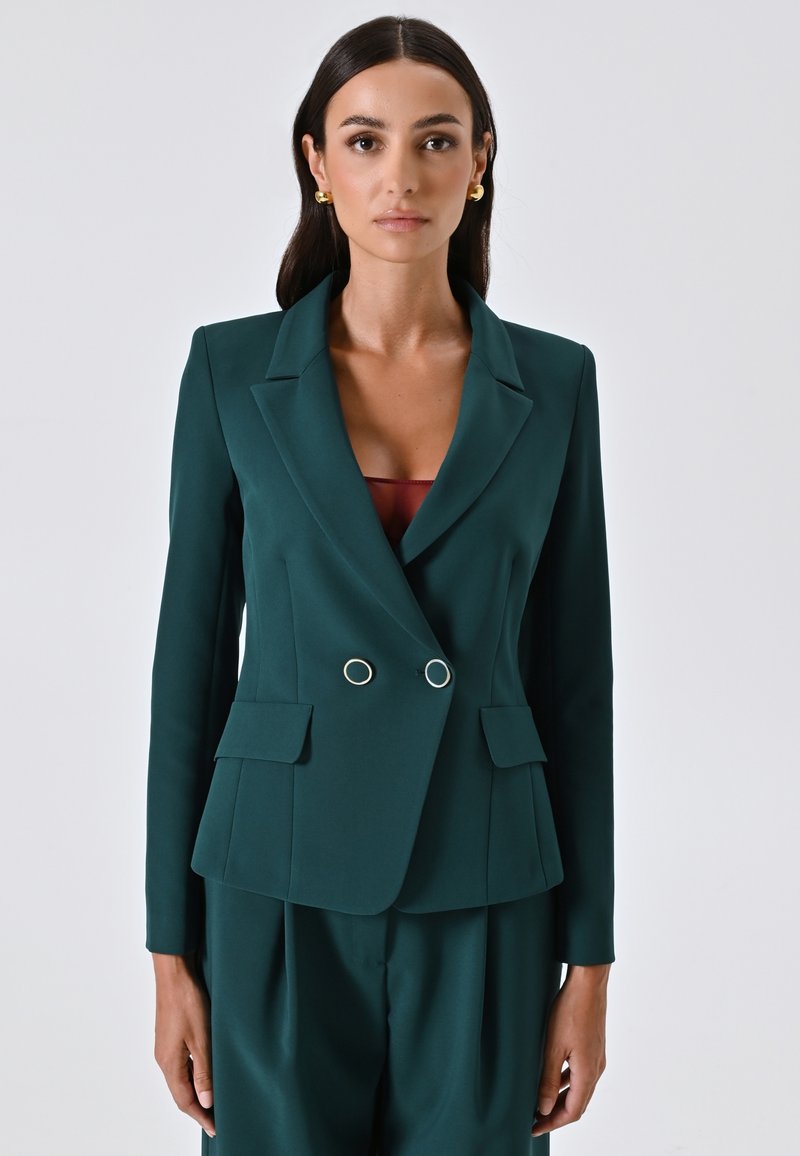 Blazer su misura verde scuro con design doppiopetto, bottoni circolari argentati, due tasche frontali e rever a intaglio. Tessuto dalla texture liscia.
