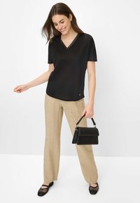 Sort kortærmet V-hals top parret med beige linnedbukser, sort skuldertaske med struktureret design og sorte mesh flade sko.