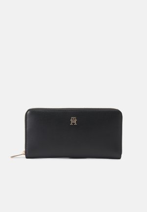 Portefeuille en cuir noir avec une surface texturée, accent de logo doré, fermeture zippée sur le dessus et forme rectangulaire fine.
