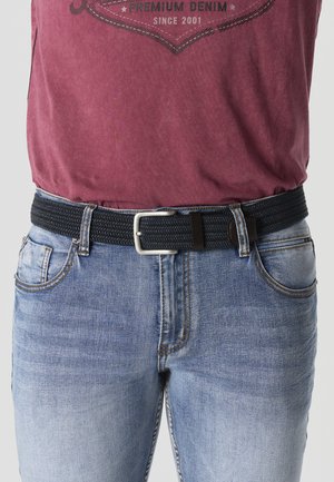 Persona vistiendo jeans azul claro con un cinturón negro tejido y una camiseta burdeos metida dentro.