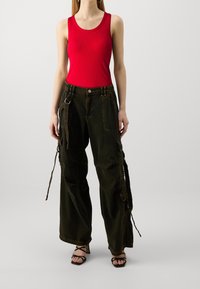 Débardeur rouge à côtes associé à un pantalon cargo vert foncé ample avec de multiples poches et des cordons ajustables. Sandales noires à lanières.