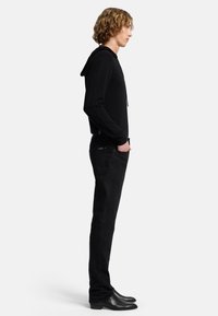 Felpa nera con cappuccio regolabile, abbinata a jeans neri slim-fit e stivaletti neri alla caviglia. Il tessuto sembra morbido e texturizzato.