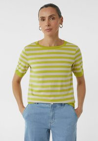T-shirt z krótkim rękawem w paski w jasnym zielonym i białym kolorze, z okrągłym dekoltem i gładką teksturą. Połączony z jasnoniebieskimi dżinsami.