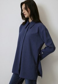 Navy blue shirt with white vertical stripes, button-down collar, long sleeves, and side slits. Features silver buttons at sleeve cuffs.