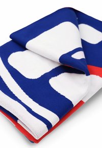 Zrobiony na drutach koc z niebieskim, białym i czerwonym abstrakcyjnym wzorem; miękka tekstura z zagiętym rogiem ujawniającym kontrastujące kolory.