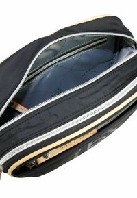 Schwarze Nylon-Tasche mit einem Hauptfach und einem Nebenfach, ausgestattet mit silbernen Reißverschlüssen, einem Innenfutter mit geometrischem Muster und Logo-Detail.