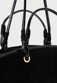Black suede handbag with glossy black handles. Features gold-tone hardware and textured accents on the handle grips.