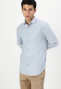 Camicia a maniche lunghe a righe azzurre con colletto a punta e chiusura a bottoni, abbinata a pantaloni beige. Tessuto dalla consistenza morbida.