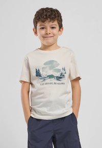 Kremowy t-shirt z krótkim rękawem, z grafiką błękitnego krajobrazu górskiego i niedźwiedzia oraz napisem "TINY NOMADS, BIG DREAMS." Wykonany z miękkiej bawełny.