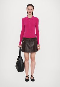 Pull fuchsia à boutons, mini-jupe en cuir, sac à main noir avec accents zippés, et chaussures plates à brides croisées noires.