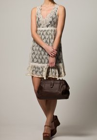 Kermakuvioinen pitsimekko, jossa on V-pääntie ja aaltoilevat reunat, yhdistettynä tummanruskeaan nahkalaukkuun, joka on muotoilultaan sääntömääräinen ja jossa on kultaiset yksityiskohdat.