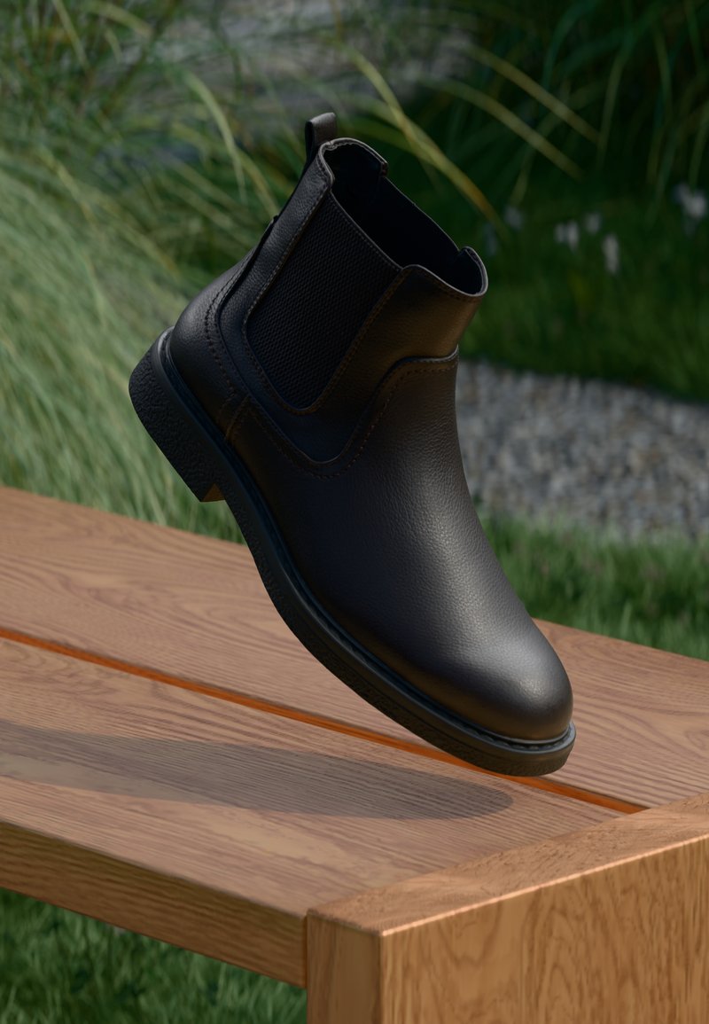 Black leather ankle boot with elastic side panels, smooth texture, rounded toe, and low rubber sole, suspended above a wooden surface.