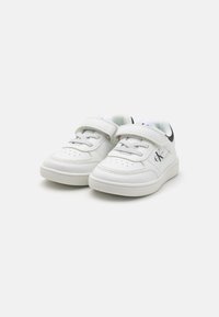 Baskets en cuir blanc avec un bout perforé, une sangle Velcro et un logo sur le côté. Semelle en caoutchouc plate et doublure intérieure douce.