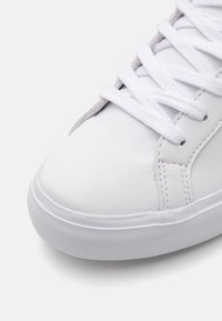 Fehér sneaker sima bőr felsőrésszel. Kerek orral, lapos fehér fűzőkkel és texturált gumitalppal rendelkezik, tiszta dizájnnal.