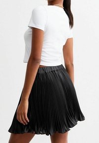 Zwarte geplooide rok met een aansluitende tailleband, gemaakt van een glanzend materiaal, gecombineerd met een wit T-shirt met korte mouwen.