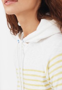 Haut à capuche blanc avec des rayures jaunes, doté d'un cordon de serrage avec des accents bleus. Texture de tissu douce, col rond et poignets côtelés.