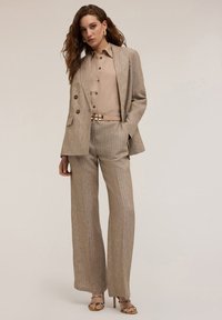 Traje beige a rayas con un blazer a medida y pantalones de pierna ancha, combinado con una blusa clara y un cinturón beige con un cierre metálico.