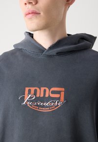 Sudadera con capucha en tejido gris oscuro con una textura desgastada. Presenta un logo bordado en naranja y plata que dice "Paradise Disco Dancing Club".