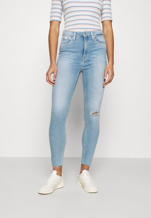 Dopasowane jasnoniebieskie dżinsy z podartym kolanem, z postrzępionymi brzegami, noszone z białymi trampkami i pasiastą bluzką z krótkim rękawem.