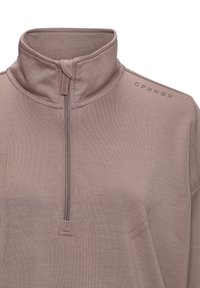 Pusē ar rāvējslēdzi izgatavots no mīksta mauve auduma. Satur stāvošu apkakli, smalku tekstūru un "CPHNGN" zīmolu plecā.