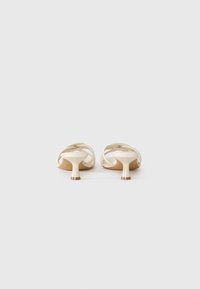 Beige mules avointé dengan desain tali silang, bagian atas plastik halus, dan tumit silindris pendek dengan dasar mirip kayu.