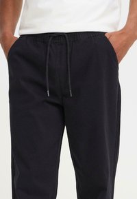 Los pantalones negros con cordón presentan un corte relajado, una cintura elástica y bolsillos laterales, fabricados con una suave y ligera tela de algodón.