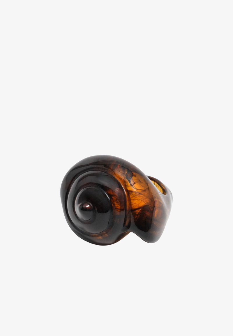 Anillo de resina ámbar oscuro con forma de espiral de concha de caracol, con superficie lisa y pulida sobre un fondo blanco.
