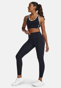 Schwarzer Sport-BH mit weißen Details und Leggings aus einem glatten, dehnbaren Material. Weiße Sportschuhe runden das Outfit ab.