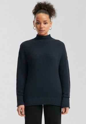 Navyblauwe coltrui met een gestructureerd breipatroon, verlaagde schouders en geribde manchetten en zoom voor extra detail.