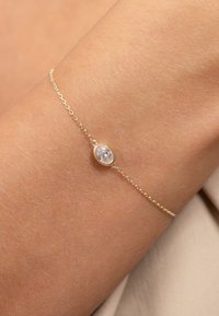 Bracelet en chaîne en or présentant une pierre précieuse taillée en ovale, sertie dans un chaton lisse, sur un fond de teint clair.