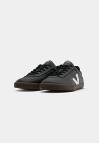 Sneakers pretos feitos de couro com uma superfície texturizada, apresentando um logótipo branco na lateral e uma sola de borracha escura. Design com atacadores.