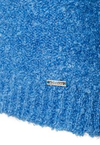 Blaues texturiertes Gewebe mit einer flauschigen Oberfläche, versehen mit einem silbernen Etikett mit blauen Akzenten, das sich near dem unteren Rand des Materials befindet.