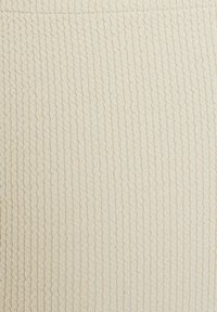 Tessuto a coste in beige chiaro, con una texture ondulata. La superficie è morbida con una leggera lucentezza, che aggiunge interesse visivo senza motivi o accenti.