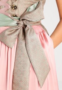 Jupe plissée rose avec un nœud à rayures vert pâle noué à la taille sur un corsage à motifs assortis avec des boutons en forme de cœur.