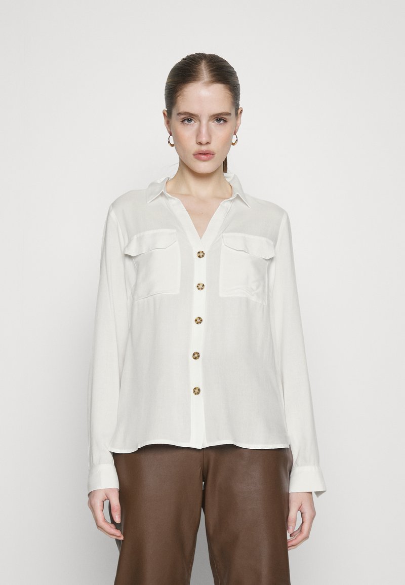 White long-sleeve shirt with a button-up front, two chest pockets, and tortoiseshell buttons. Smooth fabric with a relaxed fit.