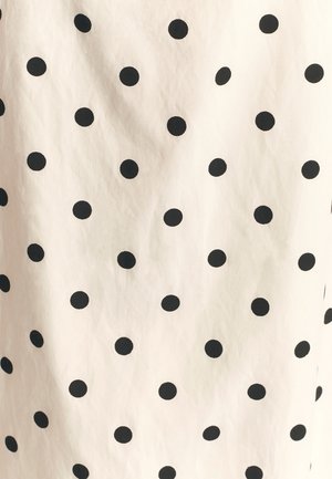 Bomuldsstof med en cremefarvet baggrund og jævnt fordelt sorte polkaprikker. Strukturen ser glat og let krøllet ud.