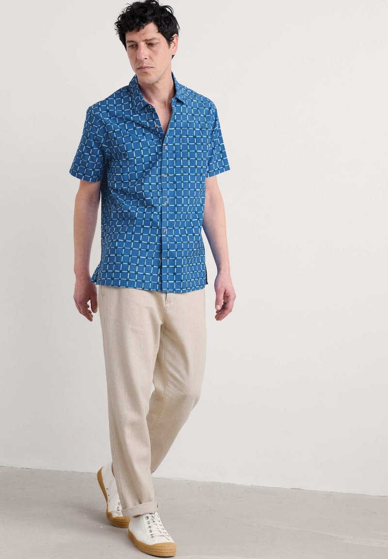 Camicia azzurra a maniche corte con motivo a quadri, pantaloni beige e sneakers bianche. La camicia presenta un colletto button-down e una vestibilità comoda.
