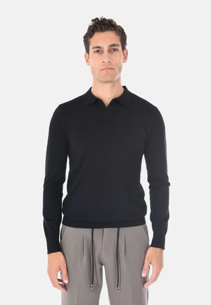 Pullover polo a maniche lunghe di colore nero con scollo a V, polsini e orlo a coste, realizzato in un tessuto liscio e leggero. Abbinato a pantaloni grigi con cordoncino.