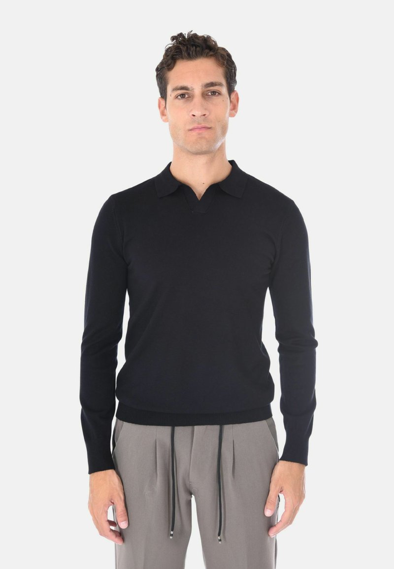 Pullover polo a maniche lunghe di colore nero con scollo a V, polsini e orlo a coste, realizzato in un tessuto liscio e leggero. Abbinato a pantaloni grigi con cordoncino.