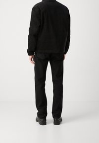 Zwarte corduroy jas met een gestructureerde afwerking, gecombineerd met zwarte spijkerbroek en zwarte schoenen. Heeft een klassieke snit met minimale details.