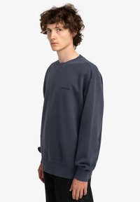 Felpa blu scuro con polsini e orlo a costine, dotata di collo a giro e discreto marchio sul petto; realizzata in morbido cotone.