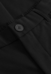 Mustast kangast, pehme tekstuuriga, mis on varustatud siledalt kinnituva nööbiga, voldikus disainiga ning nähtavate õmblusdetailidega vöökohal.