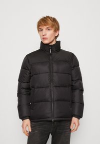 Schwarze Daunenjacke mit hohem Kragen, Reißverschluss vorne und elastischen Bündchen. Verfügt über gesteppten Abschnitte zur Isolierung und einer glatten, glänzenden Textur.