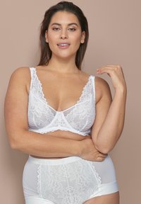 Weiße Spitzen-BH mit breiten Trägern und floralem Muster, kombiniert mit weißen hochgeschnittenen Slips, die ein ähnliches Spitzenmuster und strukturelle Akzente aufweisen.