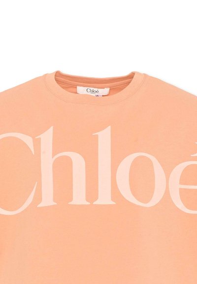 Sweat-shirt col rond couleur pêche avec un grand logo blanc "Chloé" imprimé sur la poitrine et une petite étiquette de marque en tissu à l'intérieur de l'encolure.