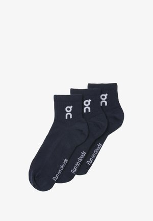 Trzy pary granatowych skarpetek na kostkę z białym logo "on" i napisem "Run on clouds" z boku, ułożonych w nakładaniu na sobie na białym tle.