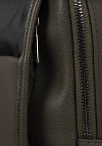 Mochila verde oliva con un exterior de cuero texturizado y una parte superior de tela tejida. Accesorios de cremallera negra con un detalle de tirador suave.