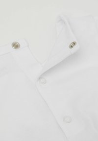 Bílá bavlněná košile se zapínáním na knoflíky, texturovaná látka a hladký povrch, který zdůrazňuje jednoduchost designu.